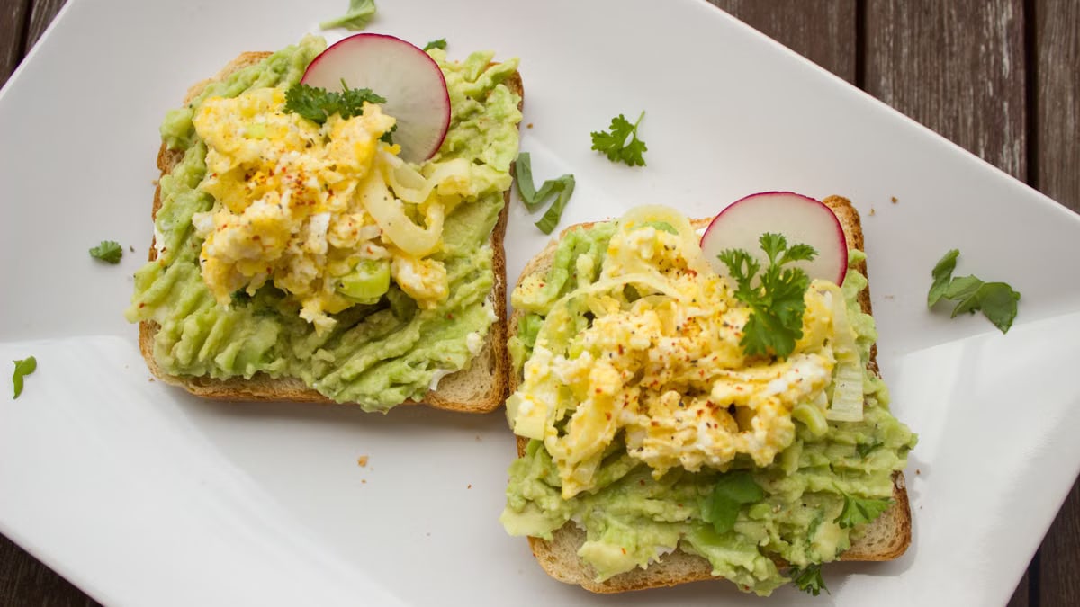 Deliciously prepared avocado and egg sandwiches garnished with radish on a white plate.